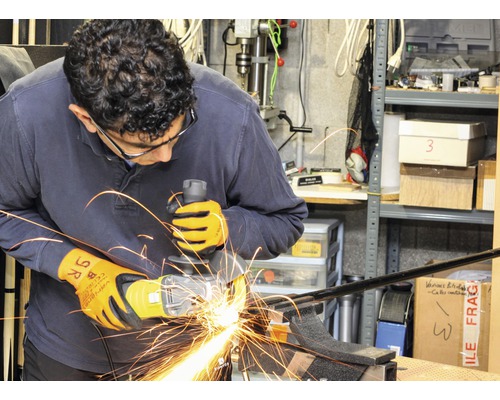 Ein Mann schleift Metall mit einem Winkelschleifer, während er Schutzhandschuhe und eine Schutzbrille trägt.