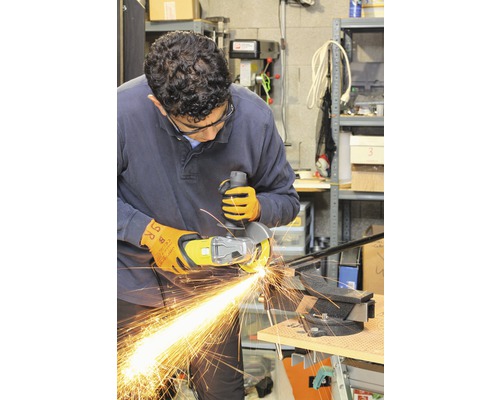 Ein Mann benutzt einen Winkelschleifer mit Funkenflug an einem Werkstück, das in einem Schraubstock befestigt ist