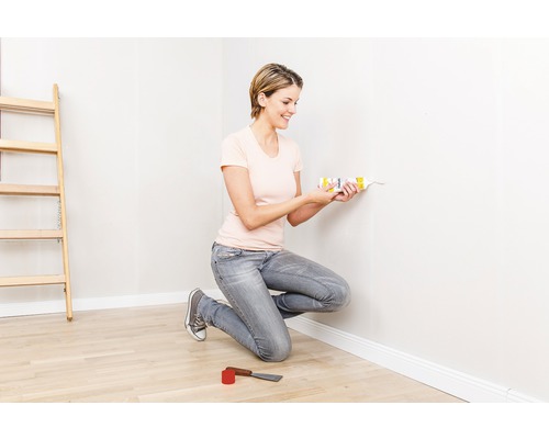 Moltofill innen Reparaturspachtel 360 g +10% gratis! Frau verwendet Dichtstoff aus der Kartusche an einer Wand in einem Raum mit Leiter