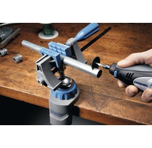 Dremel Logo. Werkbank mit Dremel Multi-Spannstock und Dremel Multifunktionswerkzeug beim Durchtrennen eines Rohres.