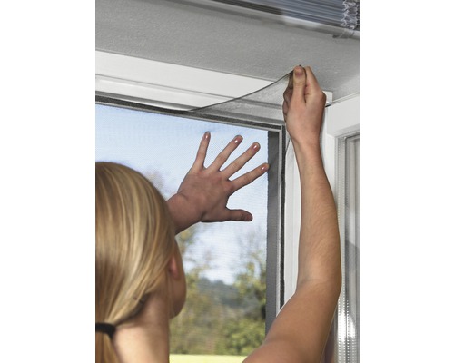 Frau befestigt ein Insektenschutzgitter an einem Fensterrahmen.