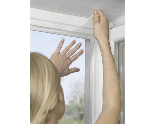 Personne fixant une moustiquaire sur un cadre de fenêtre