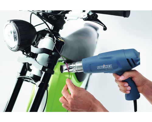 Une personne utilise un pistolet à air chaud Steinel HL 1620 S sur une moto.