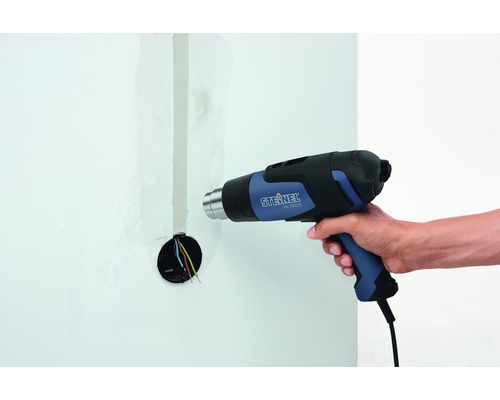 Pistolet à air chaud en main devant un mur avec des câbles exposés