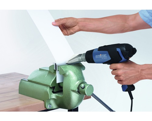 Une personne utilise un pistolet thermique Steinel pour façonner du plastique dans un étau.