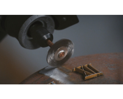 Brosse métallique montée sur une perceuse en train de dérouiller une pièce métallique