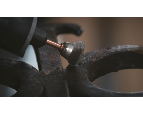 Une meuleuse avec une brosse métallique ponce une surface métallique.