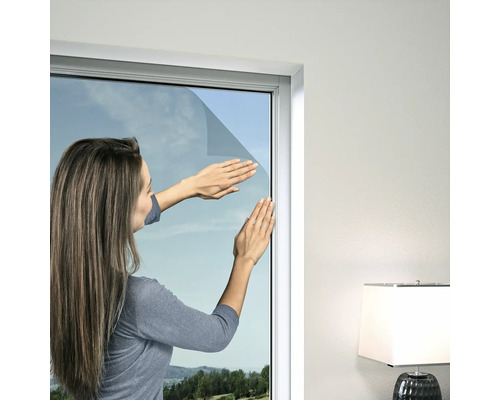 Une femme pose un film de protection solaire sur une fenêtre