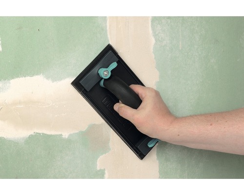 Hand schleift Spachtelmasse an einer Wand mit einem Handschleifer