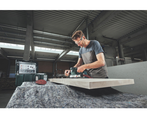 Un homme ponce une planche de bois avec une ponceuse excentrique dans un atelier.