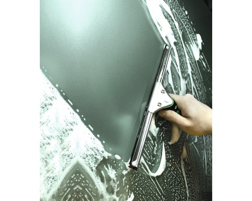 Une main essuie une surface vitrée mousseuse avec un racloir à vitre