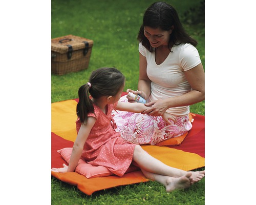 Une mère applique de la crème solaire sur le bras de sa fille dans le jardin