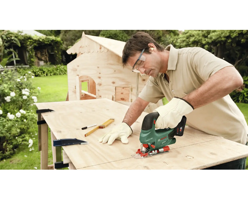 Homme sciant une plaque de bois avec une scie sauteuse pour une cabane de jeu