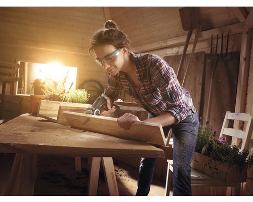 Femme travaillant avec une scie à outils multifonction dans un atelier, projet de travail du bois.