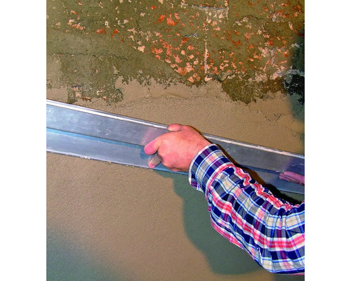 Eine Person glättet mit einer Glättkelle Putz an einer Wand.