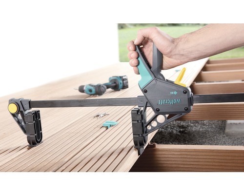 Wolfcraft Einhandzwinge auf einer Holzterrasse in der Anwendung mit einem Akkuschrauber