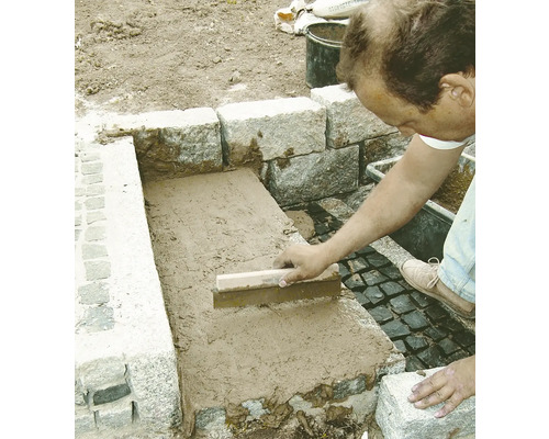 Handwerker verfugt Steine mit einem Fugenbrett im Aussenbereich.