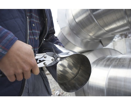 Mann schneidet ein Metallrohr mit einer Blechschere.