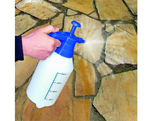 Eine Hand bedient eine Drucksprühflasche auf Steinplatten.