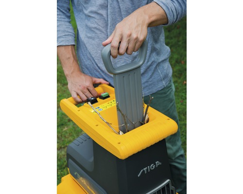 Un homme utilise un broyeur de jardin pour broyer des branches. Logo Stiga.
