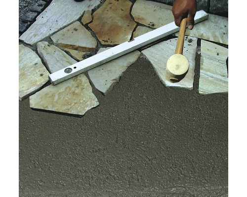 Verlegen von Natursteinplatten mit Fugenmörtel, Wasserwaage und Gummihammer.