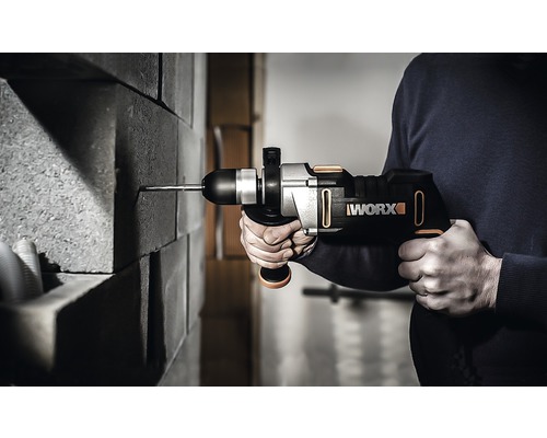 Une personne perce un mur en briques avec un perforateur sans fil. Le logo Worx est visible.