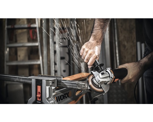 Une personne coupe une pièce métallique avec une meuleuse d''angle, qui est fixée dans un étau. Des étincelles se produisent.