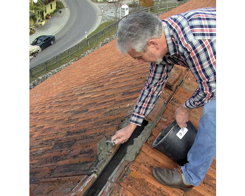 Handwerker repariert ein Ziegeldach mit Mörtel und einer Kelle.