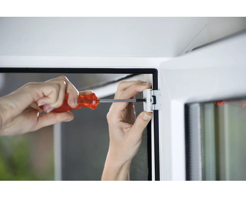 Une personne fixe une fenêtre avec un tournevis.