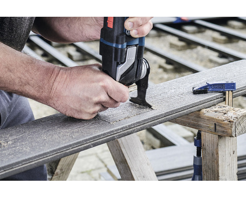 Une personne scie un trou dans une planche de terrasse avec un outil multifonction.