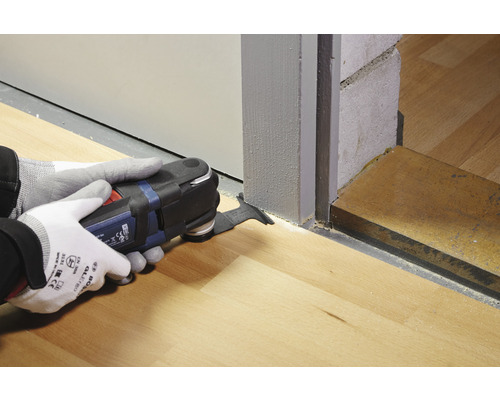 Une personne utilise un outil multifonction pour couper un plancher en bois près d''une porte.