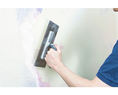 Ein Mann glättet eine Wand mit einer Glättkelle.