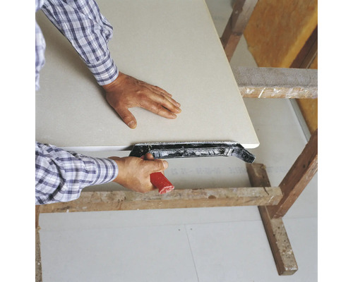 Mann glättet Gipskartonplatte mit einem Kantenhobel auf einem Holzbock