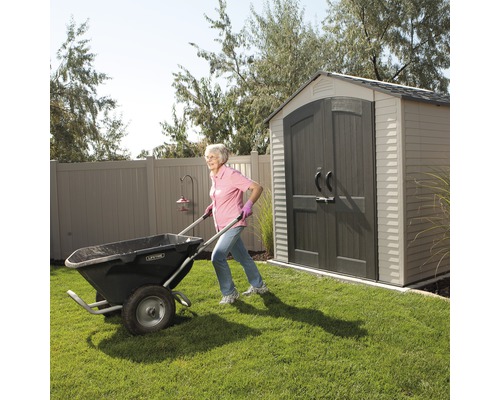 Femme poussant une brouette dans un jardin avec une remise.