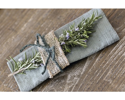Serviette décorative en tissu avec branche de romarin et corde de jute sur une table en bois.
