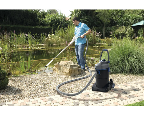 Un homme nettoie un bassin avec un aspirateur de bassin dans le jardin
