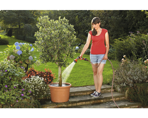 Frau giesst Baum im Topf mit Gartenschlauch im Garten