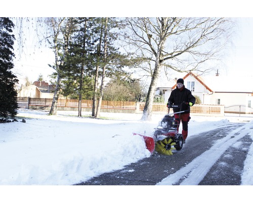 Une personne utilise une fraise à neige sur une allée enneigée.