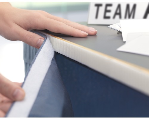 Person befestigt ein Zubehörteil mit Klettverschluss an einem Tisch