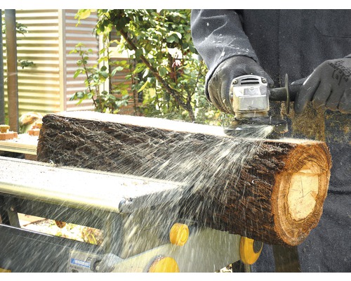 Eine Person bearbeitet einen Baumstamm mit einer Schleifmaschine auf einer Werkbank.