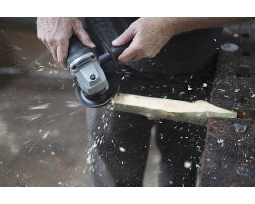 Handwerker bearbeitet Holzstück mit Winkelschleifer, Späne fliegen.