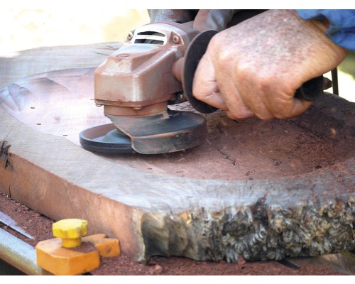 Eine Person schleift ein Holzstück mit einem Winkelschleifer.