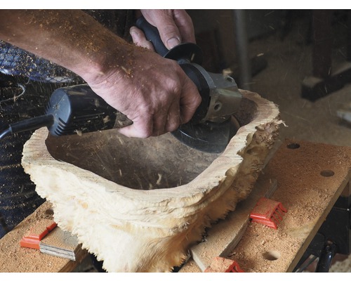 Eine Person bearbeitet eine Holzschale mit einem Winkelschleifer.