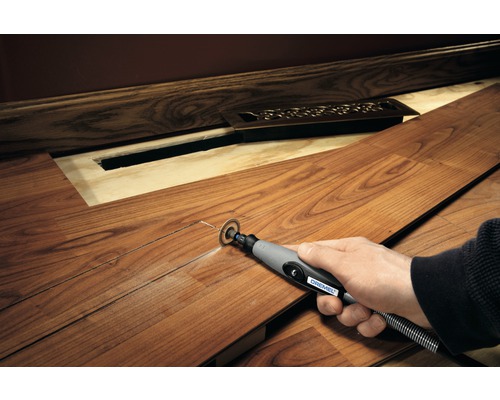 Une personne coupe une planche de stratifié avec un outil multifonction Dremel pour laisser de la place à un radiateur.