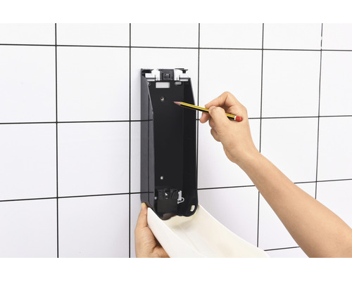 Montage eines Seifenspenders an einer gefliesten Wand mit Bleistiftmarkierung.
