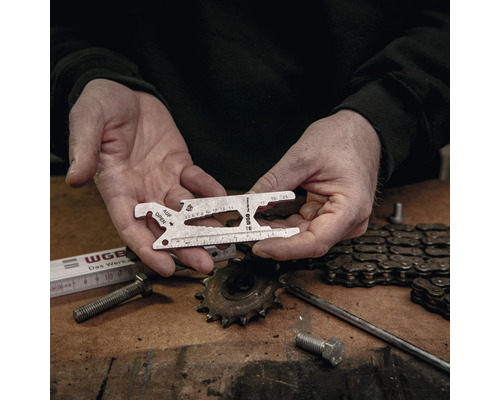 Mann hält ein Universalwerkzeug in den Händen vor einer Werkbank mit Werkzeugen.