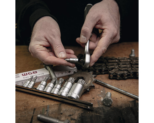 Ein Mann benutzt einen Ratschenschlüssel mit einem Bit-Set auf einer Werkbank mit Werkzeugen und Ketten.