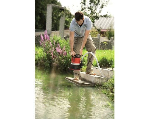 Un homme utilise une pompe à eau sale au bord d''une étendue d''eau.