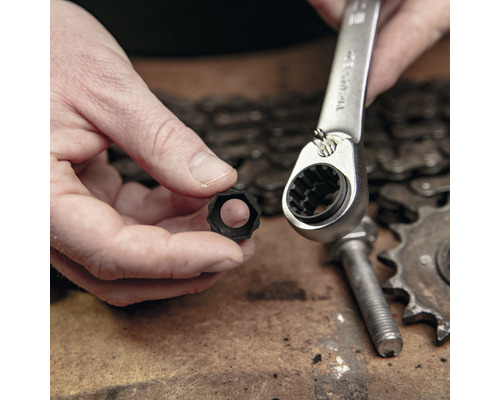 Eine Person hält einen Steckschlüsseleinsatz und eine Ratsche über einem Tisch mit einer Kette, einem Zahnrad und einer Schraube.