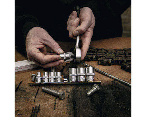 Un homme fixe une douille sur un cliquet au-dessus d''un jeu de douilles sur une table.